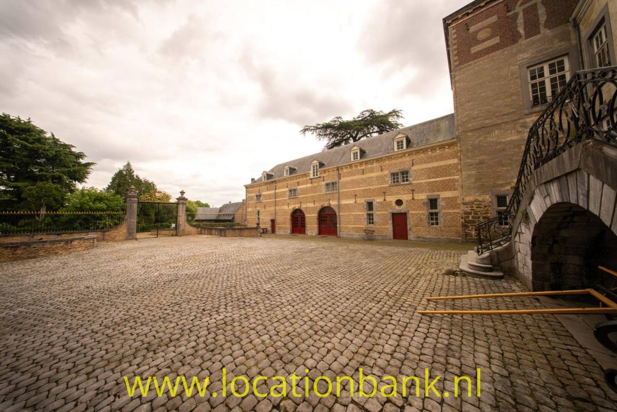Ein gepflasterter Innenhof mit einem großen Backsteingebäude, roten Türen und einem Turm.