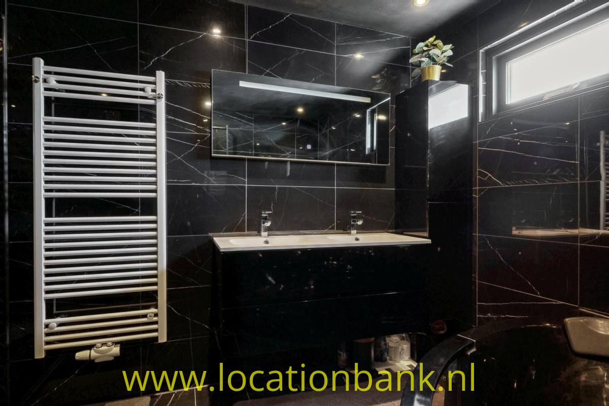 Badezimmer mit Doppelwaschbecken, schwarzen Fliesen in Marmoroptik, einem Spiegel und einem weißen Handtuchheizkörper.