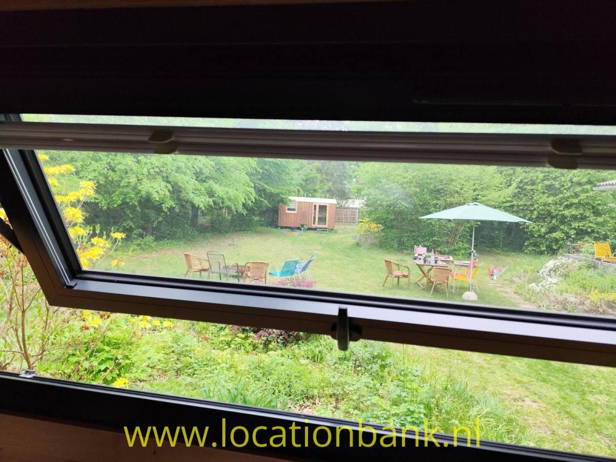 Ein Dachfenster bietet Ausblick auf einen grünen Garten mit Gartenmöbeln, Sonnenschirm und Holzschuppen.