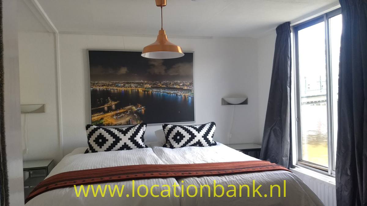 Schlafzimmer mit einem bezogenen Doppelbett, schwarz-weißen Kissen und einem Stadtfoto an der Wand.