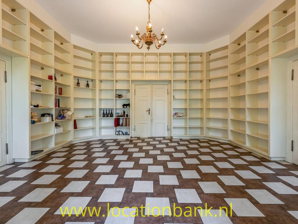 Geräumiger Raum mit eingebauten offenen Bücherregalen, Doppeltüren, einem Kronleuchter und einem geometrisch gemusterten Boden.