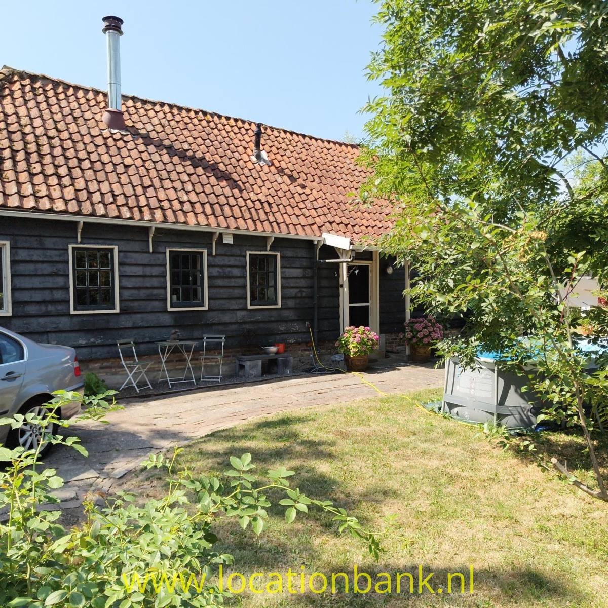 Dunkles Holzhaus mit einem roten Ziegeldach, Schornstein, Terrasse und Garten.