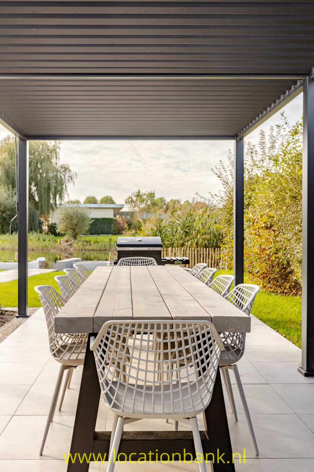 Überdachte Garten Terrasse mit langem Holzesstisch und geflochtenen Stühlen, umgeben von einem grünen Garten.