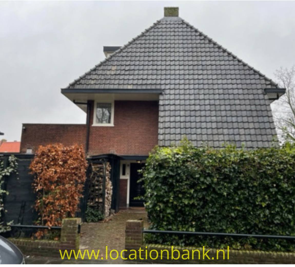 Freistehendes Haus mit großem grauem Ziegeldach, Backsteinfassade, Vorgarten und überdachtem Eingang.
