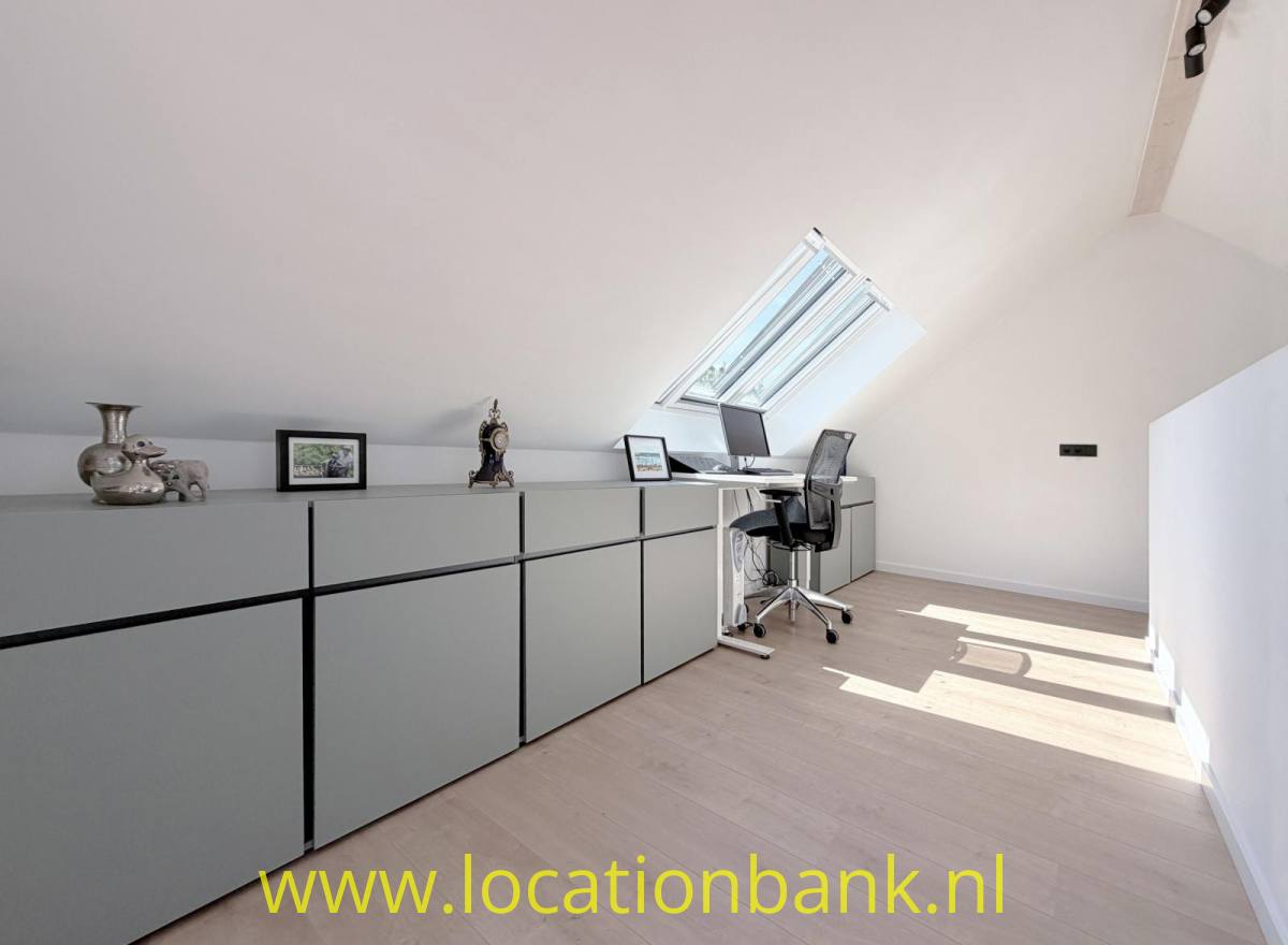 Lange niedrige Schrankwand in einem hellen Dachraum mit einem Dachfenster, Schreibtisch und Bürostuhl.
