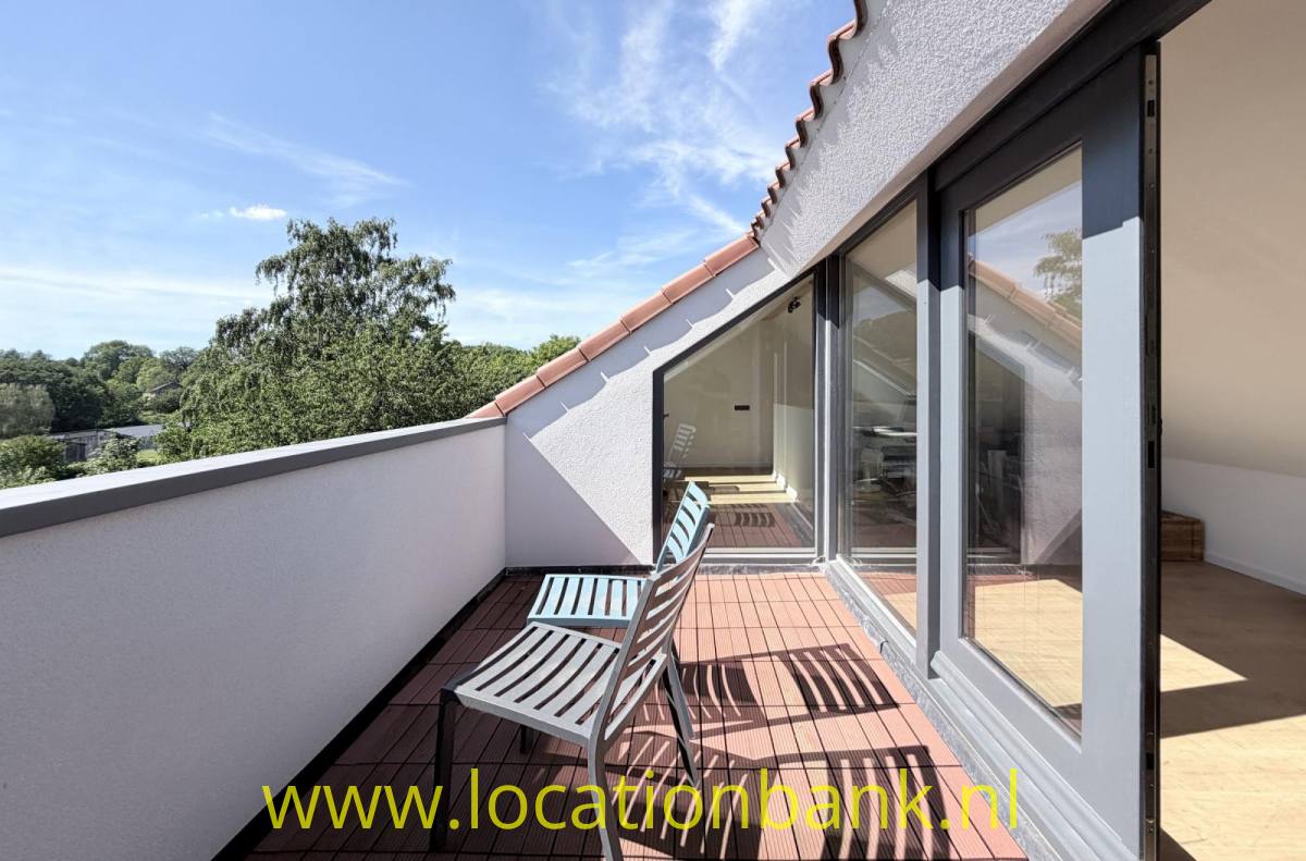 Dachterrasse mit zwei Liegestühlen, Glasschiebetüren und Blick auf Bäume und Hügel.