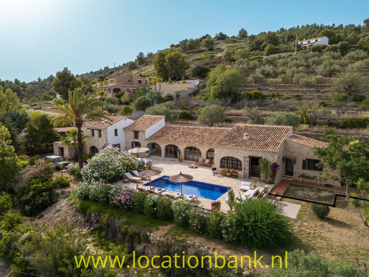 Villa in Spanien mit Terrakotta-Dachziegeln, Swimmingpool und Terrassen zwischen Olivenbäumen auf einem bewaldeten Hang.