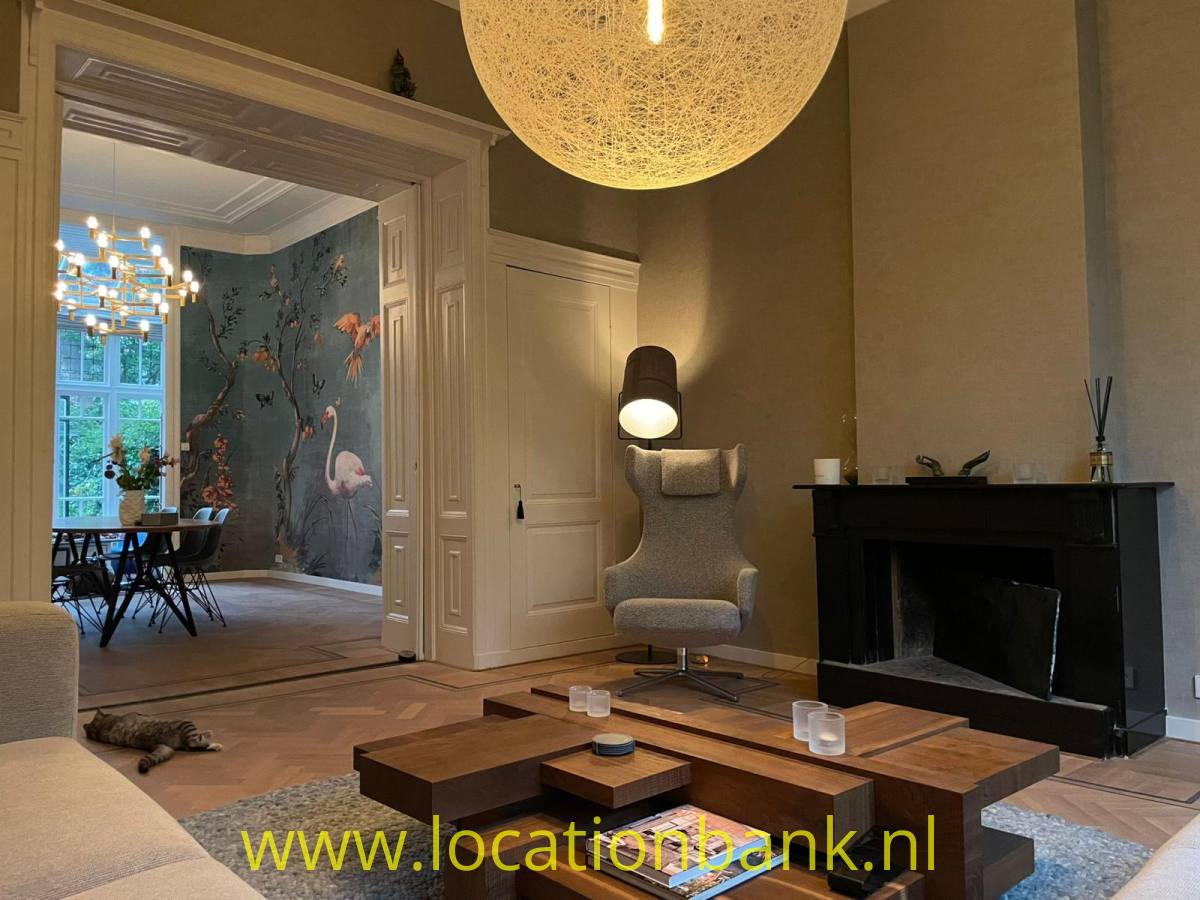 Wohnzimmer mit einem schwarzen Kamin, einem hölzernen Couchtisch, einem Sessel und angrenzendem Esszimmer mit gemusterter Tapete.