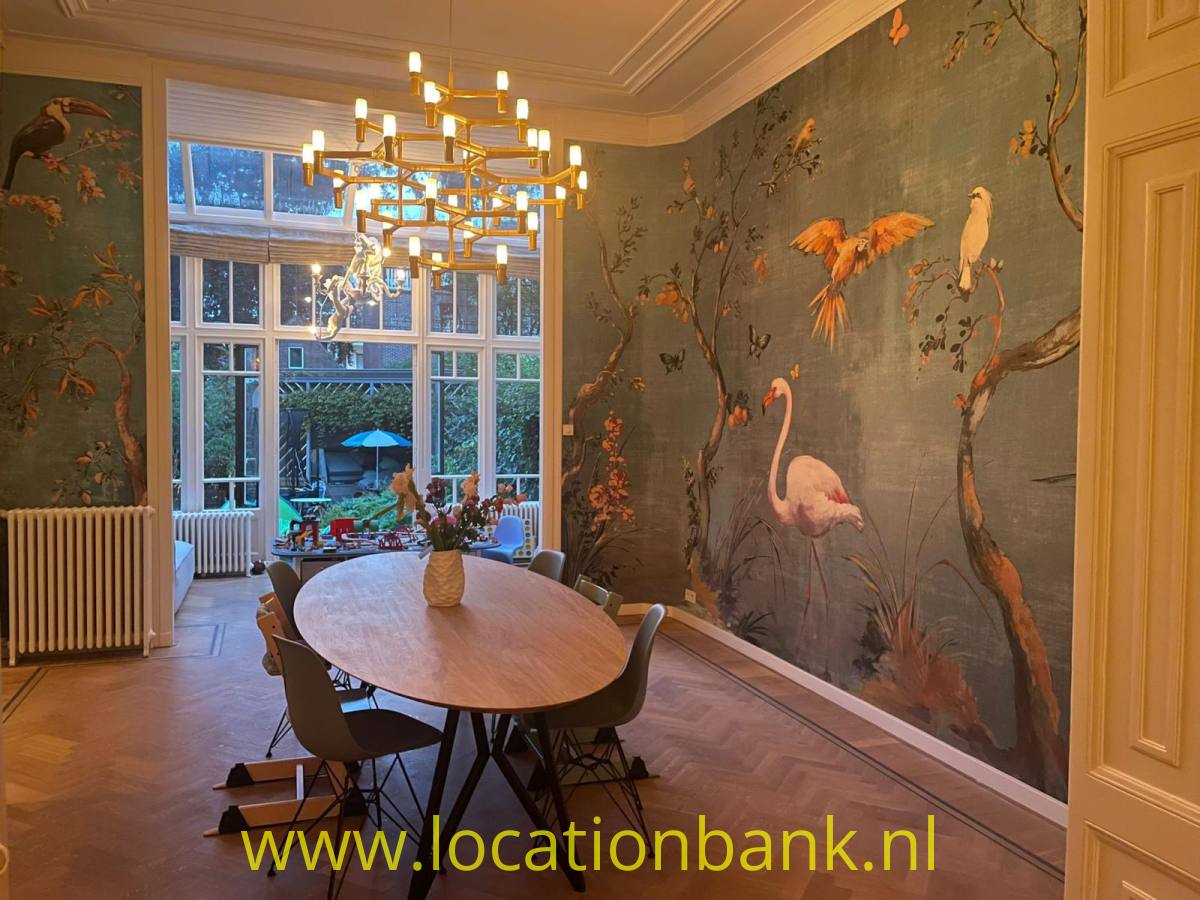 Esszimmer mit einem ovalen Holztisch, einem Kronleuchter und einer Tapete mit Vogelmotiven.