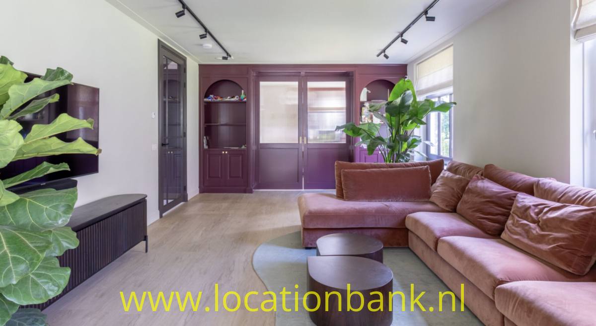 Wohnzimmer mit einem rosafarbenen Ecksofa, runden Holzcouchtischen, großen Pflanzen und dunklen Holzschränken.
