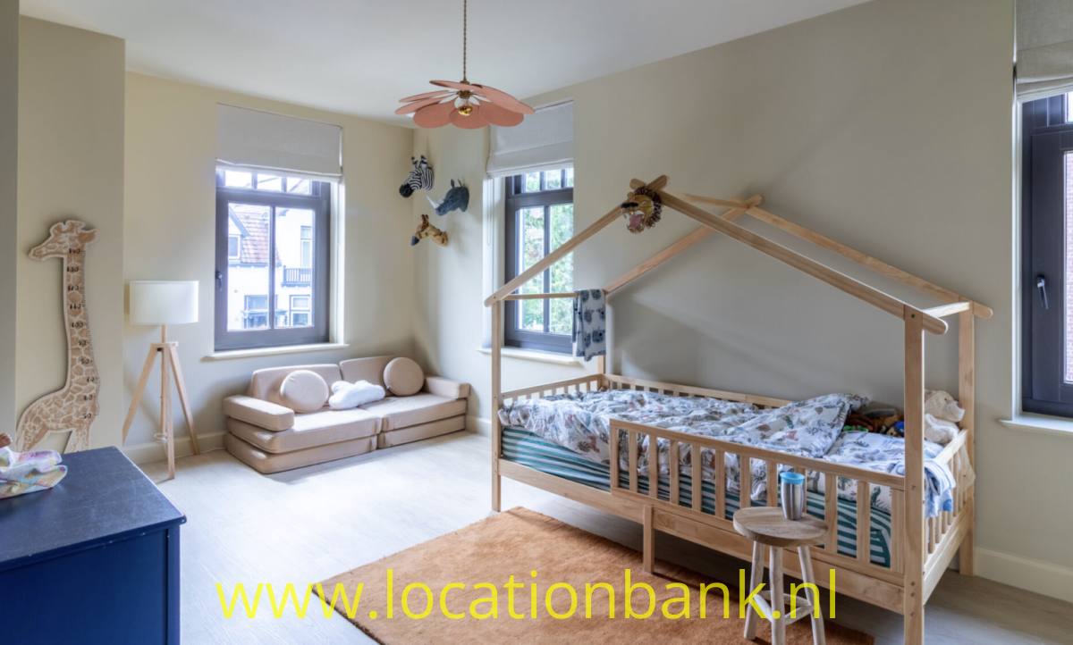 Holzbett mit hausförmigem Rahmen, blauer Bettwäsche und einem Hocker in einem hellen Zimmer.