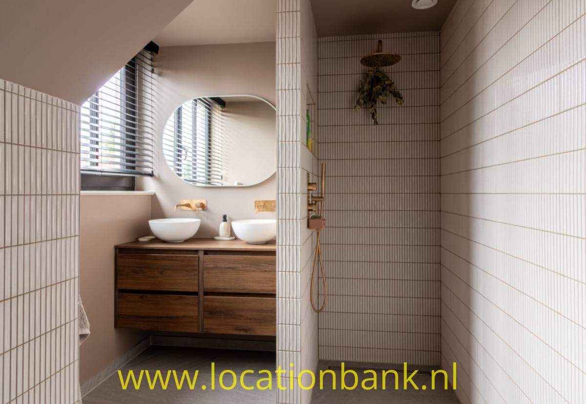 Badezimmer mit zwei Waschbecken, hölzernem Waschtischunterschrank, großem Spiegel und einer gefliesten Dusche mit Regenduschkopf.