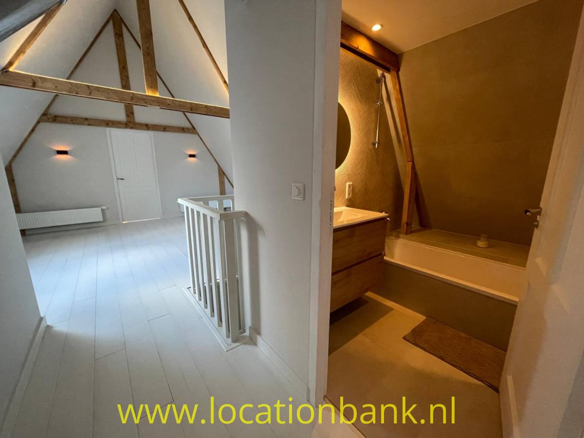 Heller Dachraum mit sichtbaren Holzbalken neben einem Badezimmer mit Badewanne.