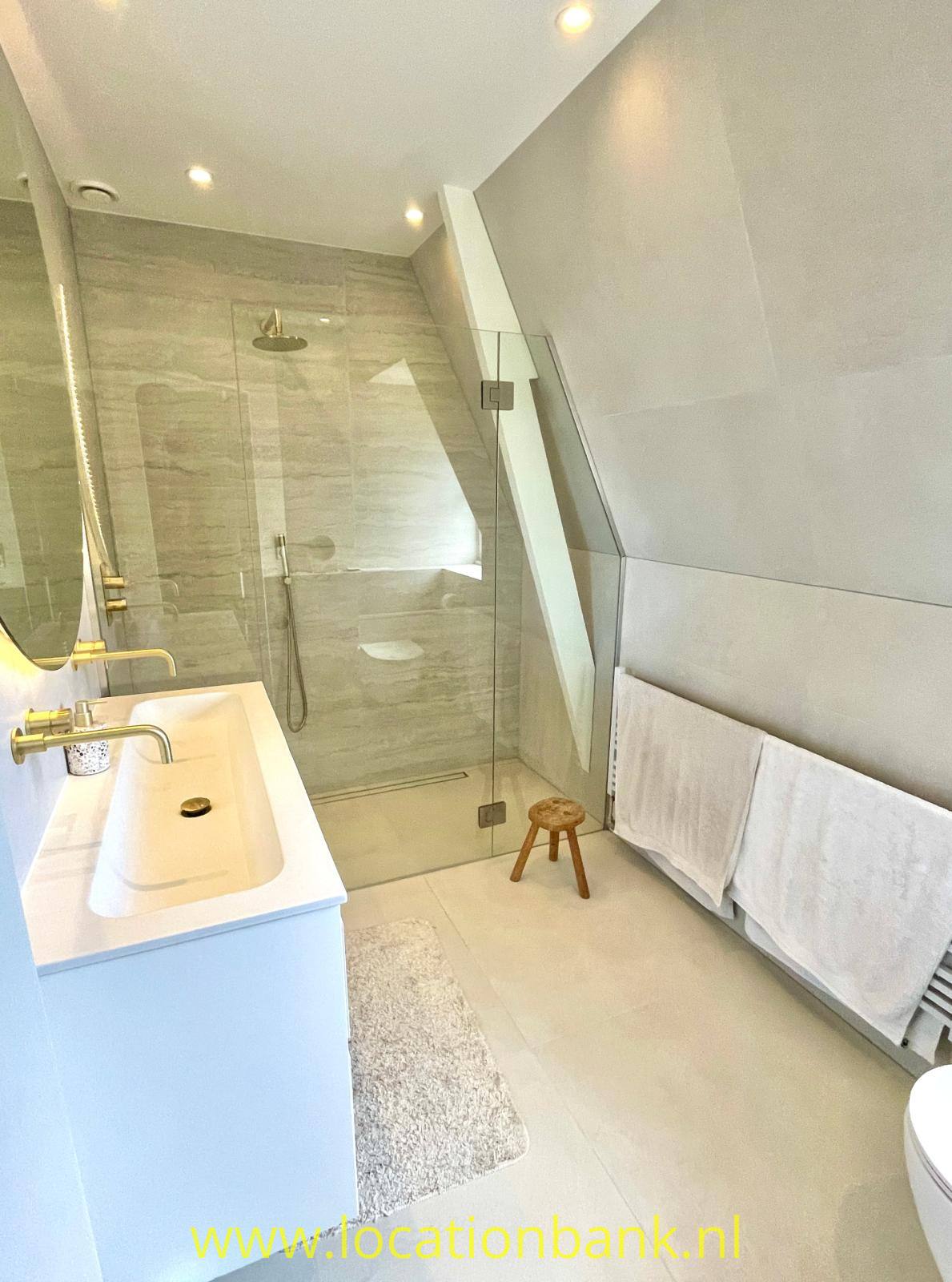 Badezimmer unter einer Dachschräge mit Glasdusche, weißem Waschtischunterschrank und Handtuchheizkörper.
