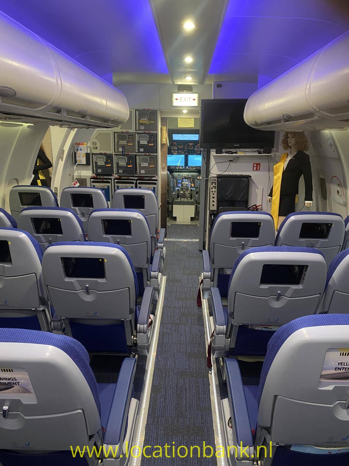 Flugzeugkabine mit Reihen blauer Passagiersitze, einem Mittelgang, Gepäckfächern und blauer Deckenbeleuchtung.