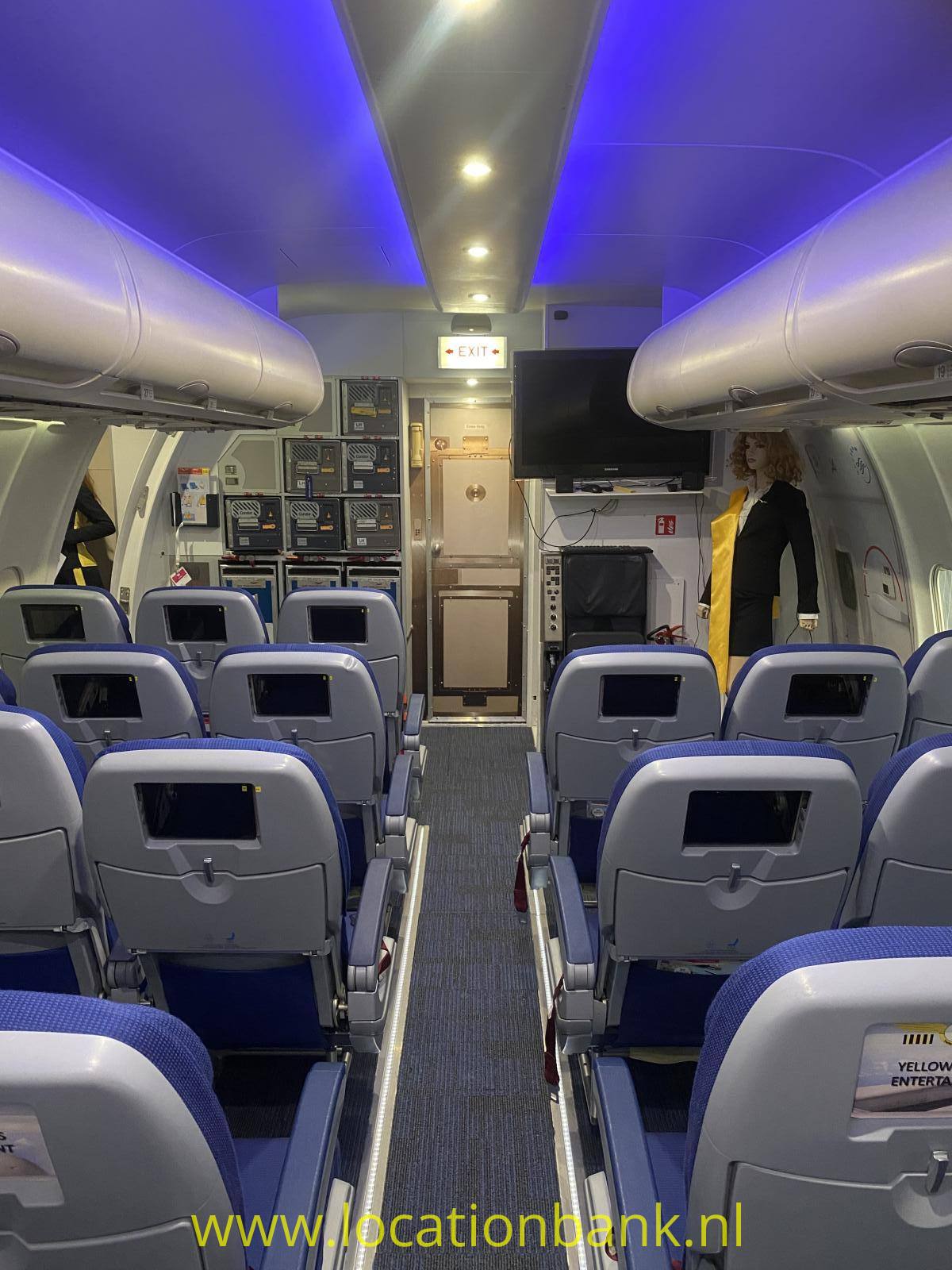 Eine Flugzeugkabine zeigt einen Mittelgang mit Reihen blauer Sitze und beleuchteten Gepäckfächern über den Passagieren.