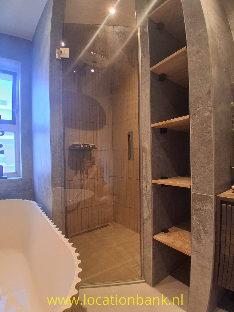 Begehbare Dusche mit Glastür, holzähnlicher Wandverkleidung und offenen Holzregalen neben einer freistehenden Badewanne.