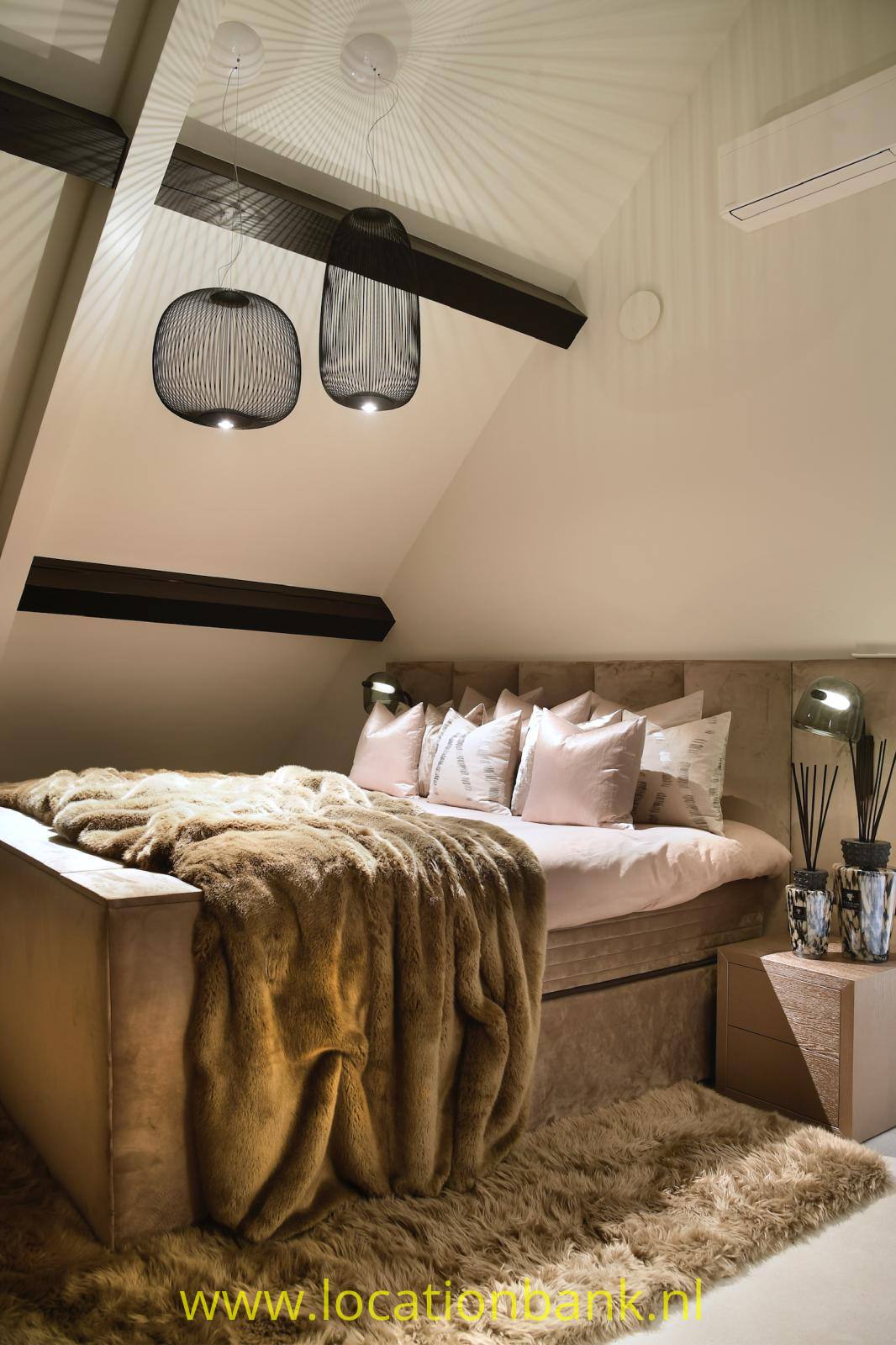 Bett mit rosa- und weißen Kissen, einer braunen Decke und Pendelleuchten unter einer schrägen Decke.