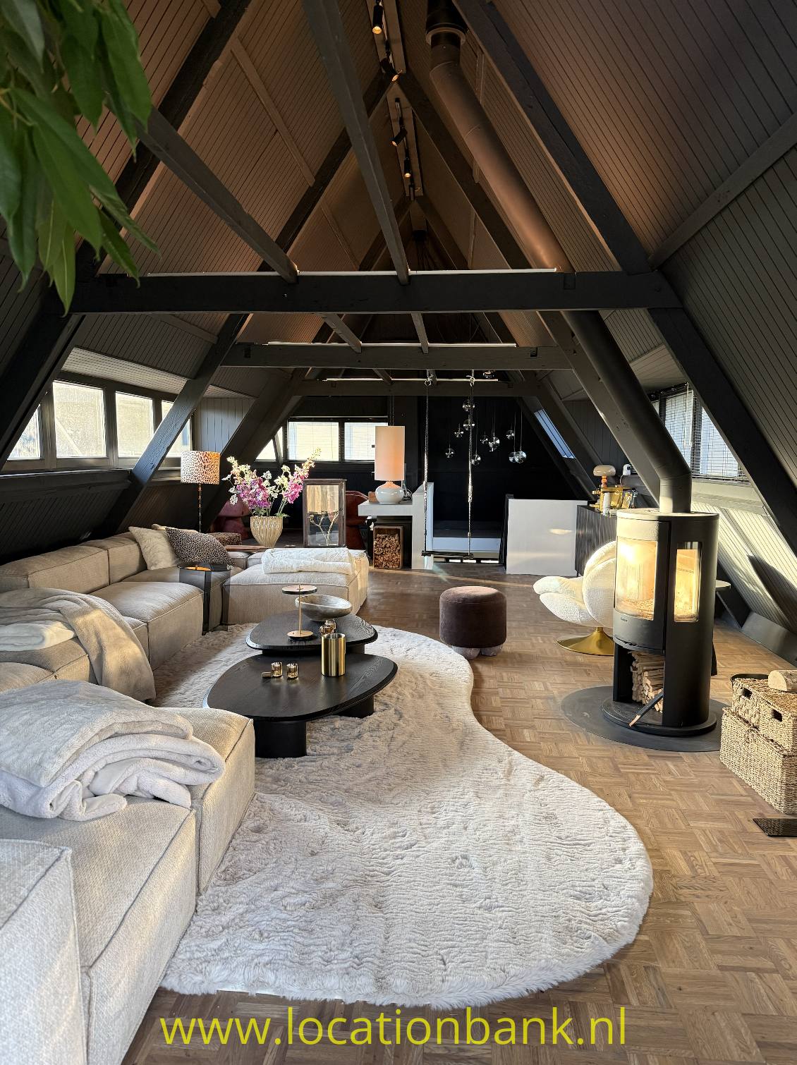 Helles Wohnzimmer unter einem schrägen Dach mit sichtbaren Holzbalken, Sitzbereich und großem Teppich.