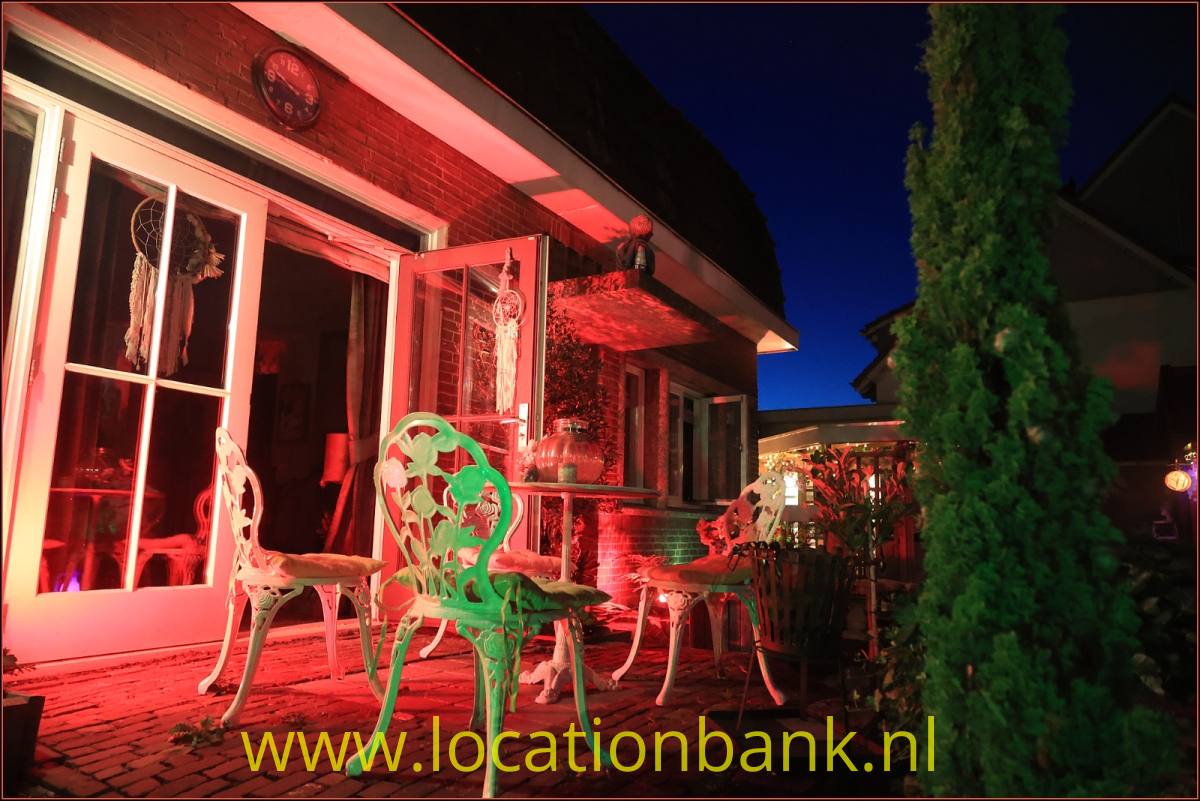 Rot beleuchtete Terrasse mit verschnörkelten Metallstühlen und geöffneten Glastüren.