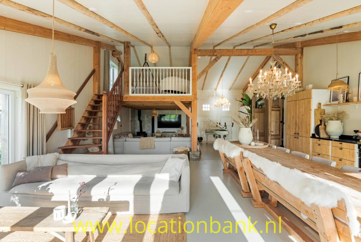 Grosse Wohnzimmer mit sichtbaren Holzbalken, einer Treppe zu einer Galerie und einem langen Esstisch.