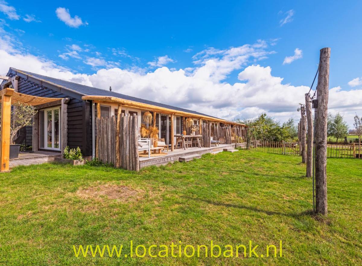 Lang gestrecktes, niedriges Holzgebäude mit überdachter Veranda, Rasenfläche und Holzzaun.