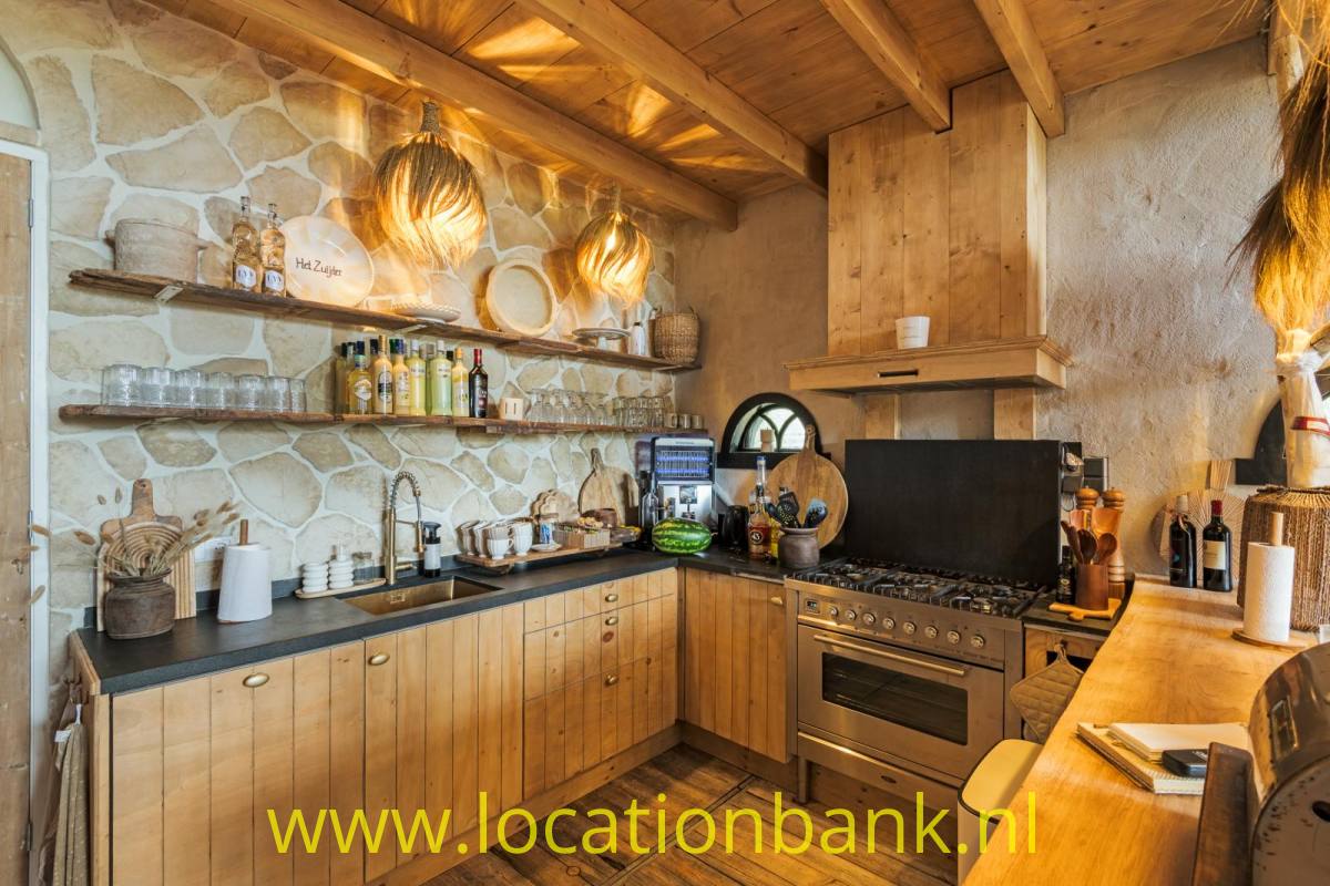 Küche mit Steinwand, Holzdecke, Herd, offenen Regalen und geflochtenen Pendelleuchten.
