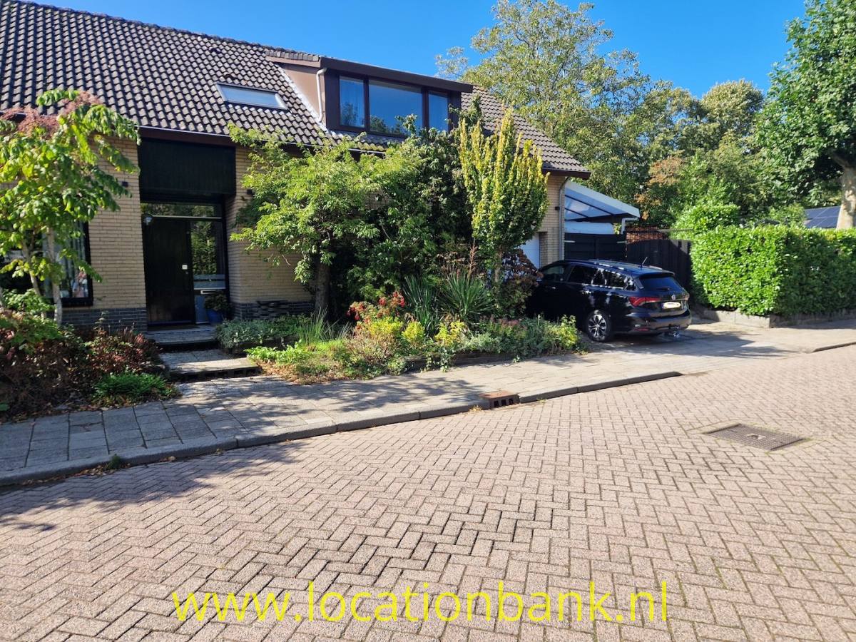 Backsteinhaus mit angebauter Garage, Vorgarten und schwarzem Auto an einer gepflasterten Straße.