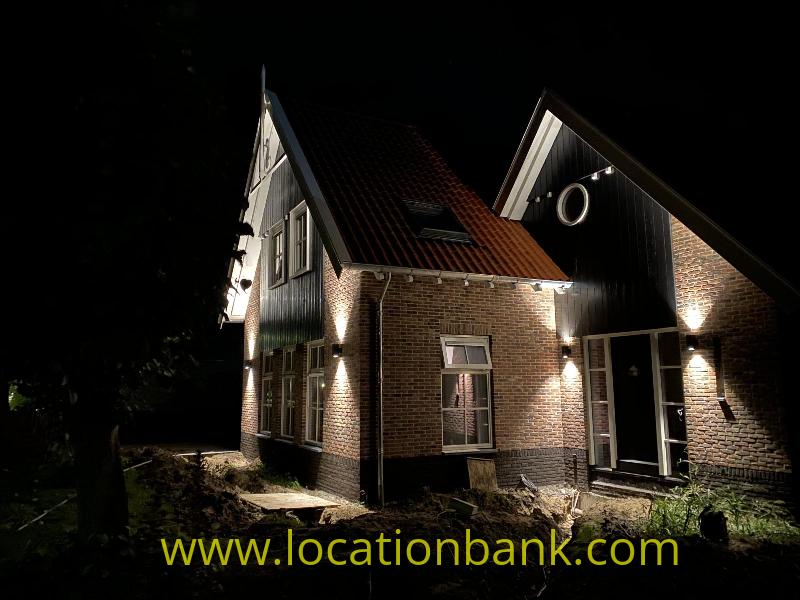Illuminated brick house with steep gabled roofs, dark timber cladding and windows at night.