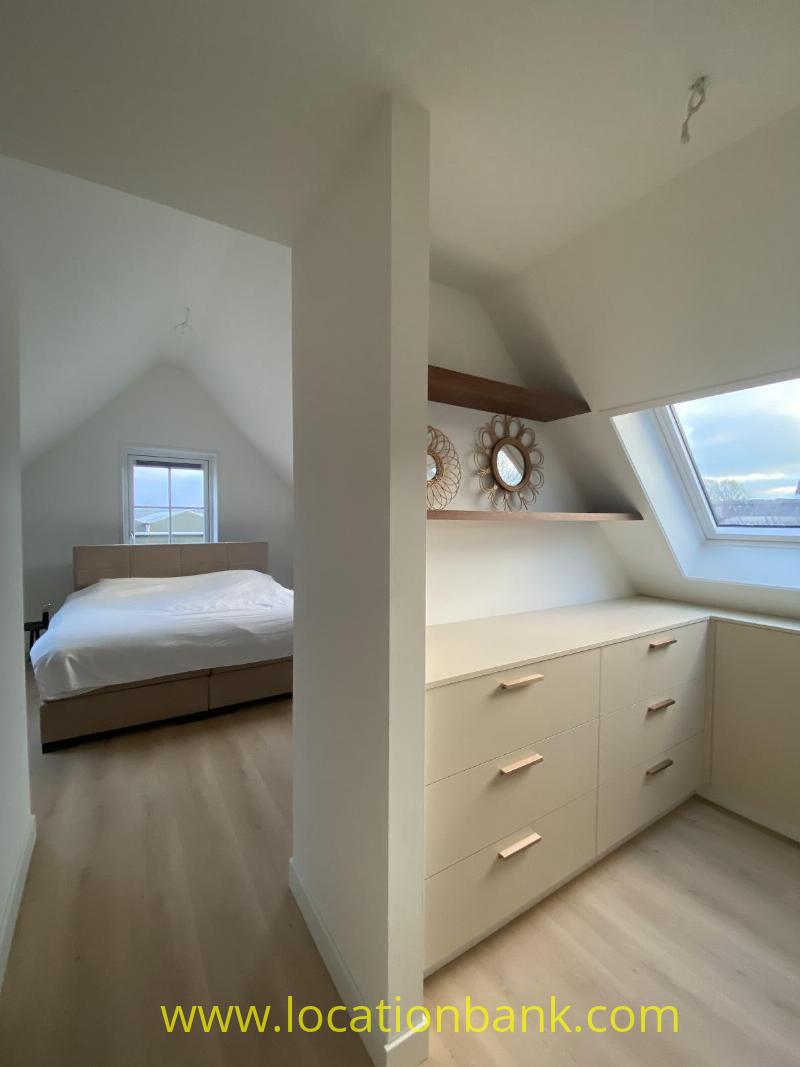 Bedroom beneath a sloping roof with a bed, built-in chest of drawers and a skylight.