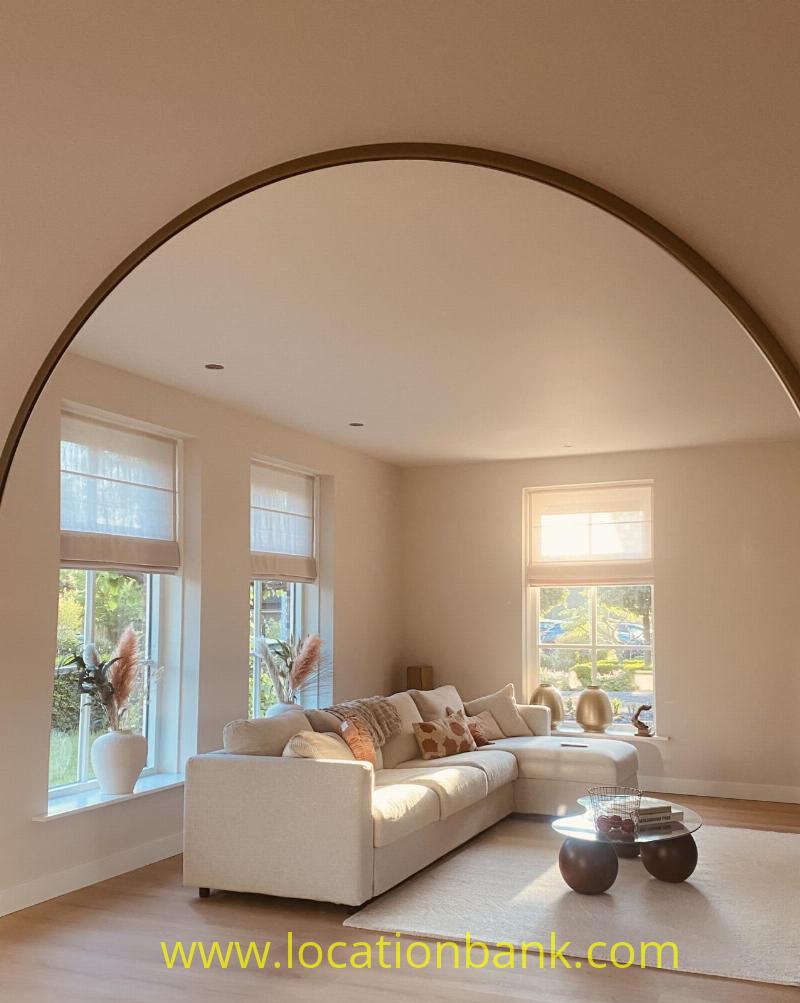 Bright living room with a cream corner sofa, tall windows and a large arched wall mirror.