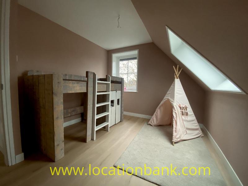 A wooden bunk bed and play tent stand beneath a large skylight in a room with a sloping ceiling.