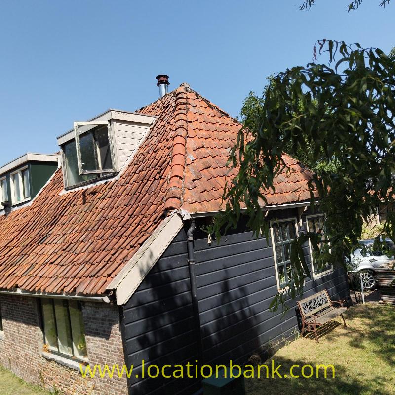 Old wooden House with a steep red tiled roof, two dormer windows, black wooden cladding 