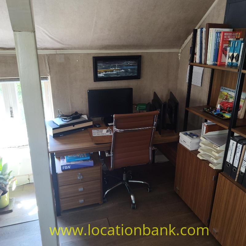 A workspace with a desk, computer monitor, keyboard, office chair and a bookcase filled with books.