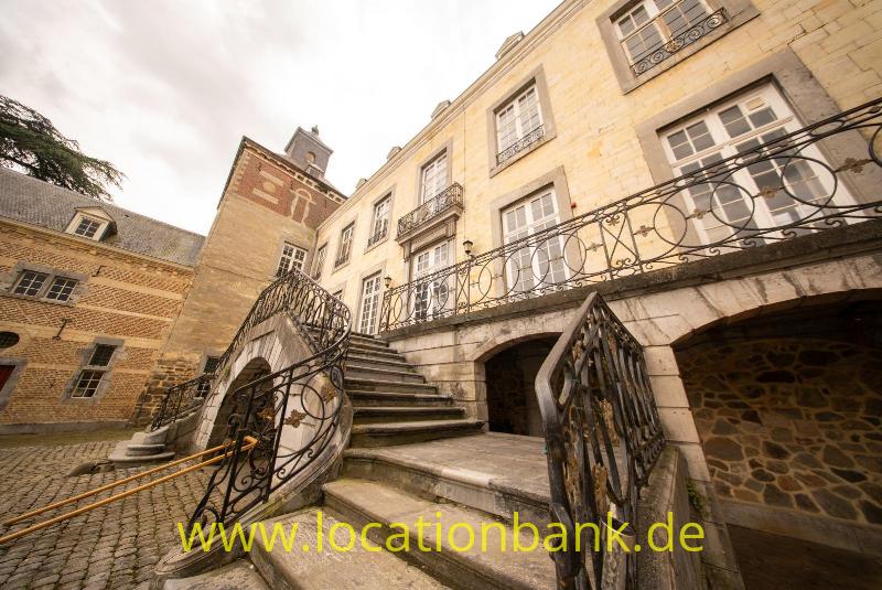 Breite Steintreppe mit schmiedeeisernen Geländern und runden Ornamenten führt zu einem Gebäude mit heller Steinfassade.