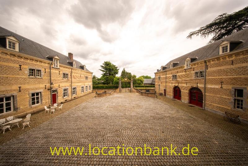 Ein gepflasterter Innenhof zwischen zwei Backsteingebäuden mit roten Türen und einem zentralen Eingangstor.