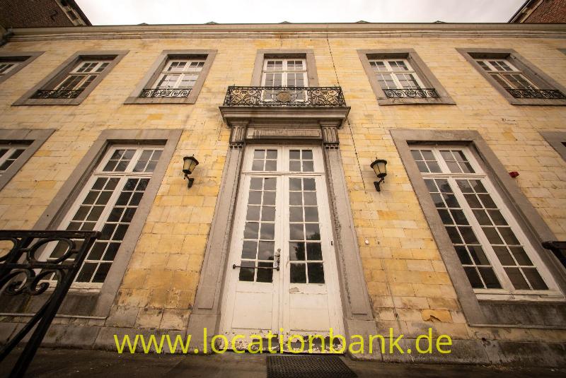 Fassade aus gelbem Stein mit hohen Fenstern, einer zentralen Doppeltür und einem schmiedeeisernen Balkon.