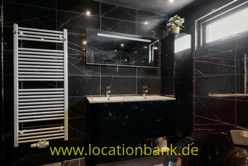 Badezimmer mit Doppelwaschbecken, schwarzen Fliesen in Marmoroptik, einem Spiegel und einem weißen Handtuchheizkörper.