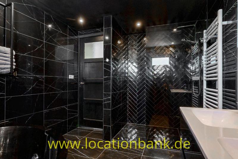 Dunkles Badezimmer mit glänzenden schwarzen Fliesen, einem weißen Waschbecken und einem weißen Handtuchheizkörper.