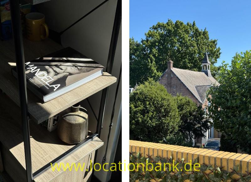 Ein offenes Regal mit Büchern und einer Tasse, daneben einer Kirche mit Turm, Bäumen und einer Ziegelmauer.