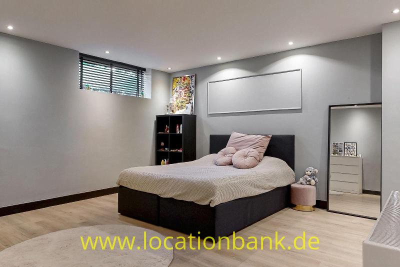 Schlafzimmer mit einem Doppelbett, einem großen Wandpaneel, einem Standspiegel und einem Fenster mit Jalousien.