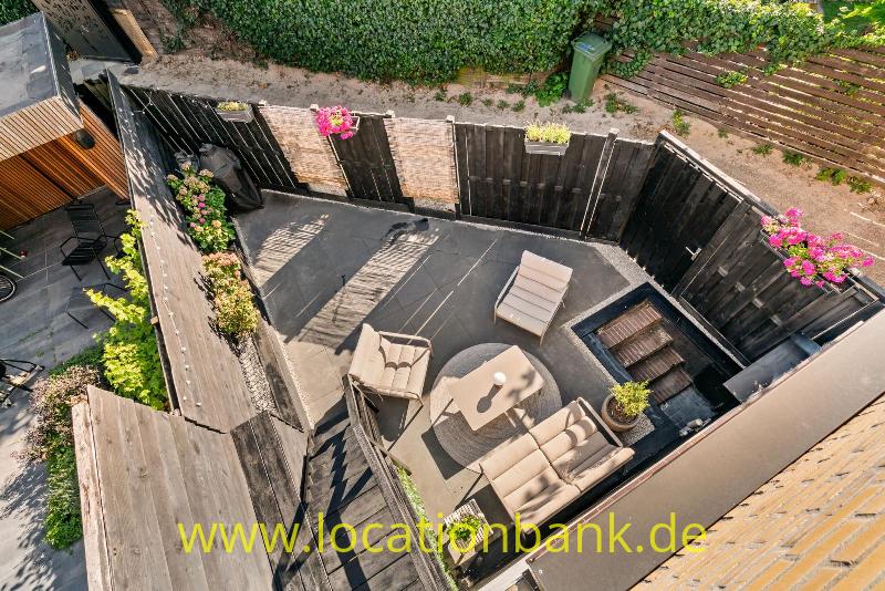 Abgeschirmte Garten Terrasse mit Sitzgruppe, Liegestühlen, Pflanzgefäßen und dunklen Holzzäunen aus der Vogelperspektive.