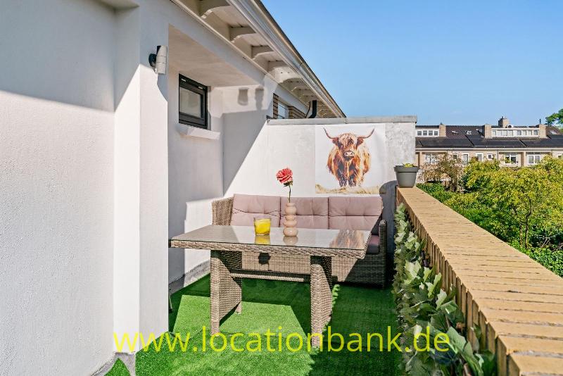 Ein Balkon mit einem geflochtenen Tisch, Sitzmöbeln, Kunstrasen, Pflanzkübeln und einem Stierbild an der Wand.