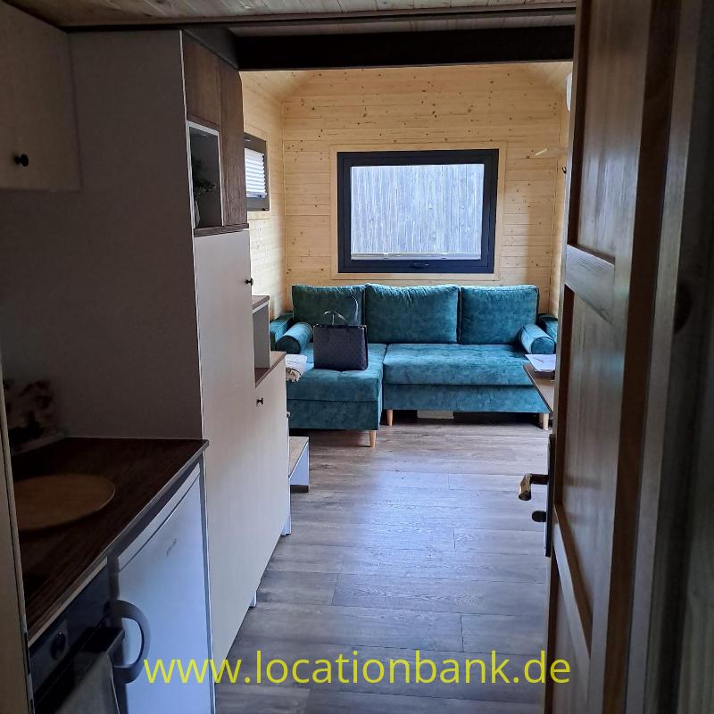 Ein blaugrünes Sofa steht an einer Holzwand unter einem Fenster, sichtbar durch eine offene Tür.