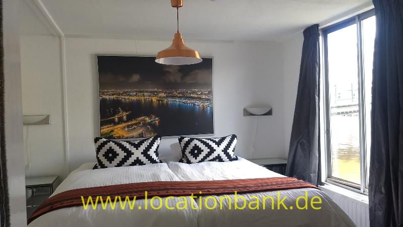 Schlafzimmer mit einem bezogenen Doppelbett, schwarz-weißen Kissen und einem Stadtfoto an der Wand.