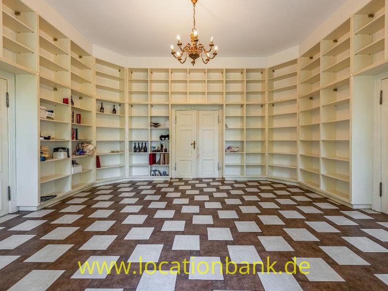 Geräumiger Raum mit eingebauten offenen Bücherregalen, Doppeltüren, einem Kronleuchter und einem geometrisch gemusterten Boden.