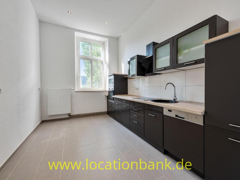Küche mit dunklen Schränken, einer hellen Arbeitsplatte, weißen Wandfliesen und einem Fenster neben dem Heizkörper.