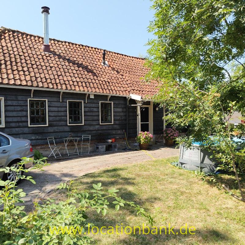 Dunkles Holzhaus mit einem roten Ziegeldach, Schornstein, Terrasse und Garten.