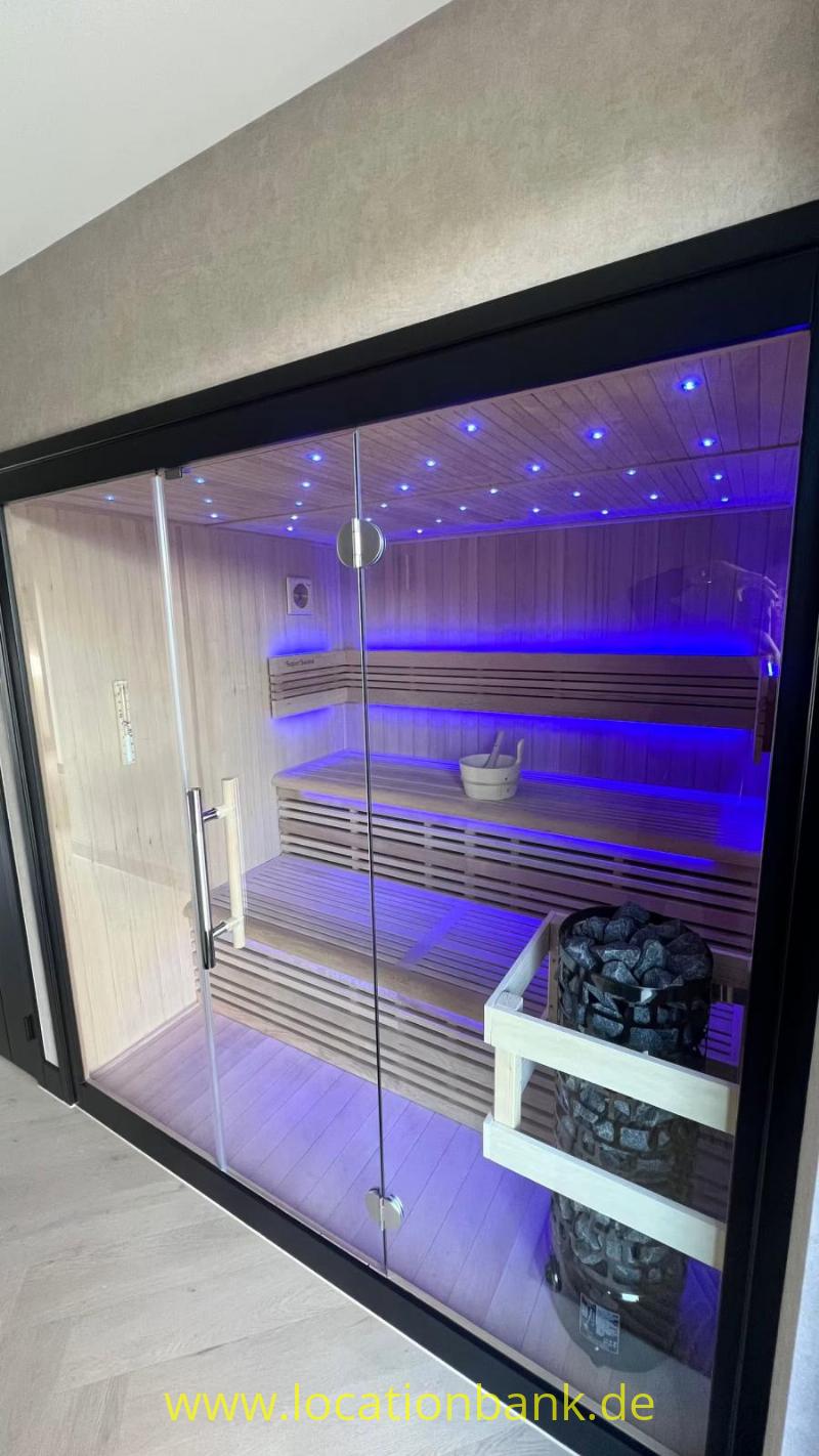 Eine Sauna mit Glasfront, Holzbänken, einem Saunaofen und violetter Beleuchtung