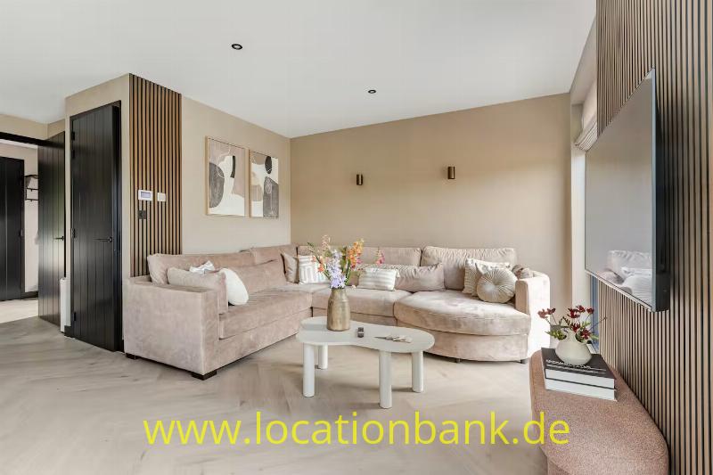 Wohnzimmer mit zwei beigefarbenen Sofas, einem ovalen Couchtisch und einer Wand mit vertikalen Holzleisten.